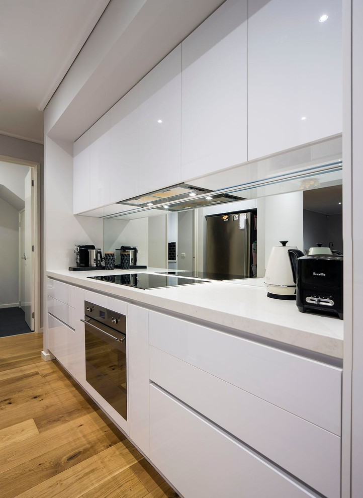 Photo of a contemporary kitchen in Melbourne with a double-bowl sink, white cabinets, granite benchtops, multi-coloured splashback, mirror splashback, stainless steel appliances and light hardwood floors.