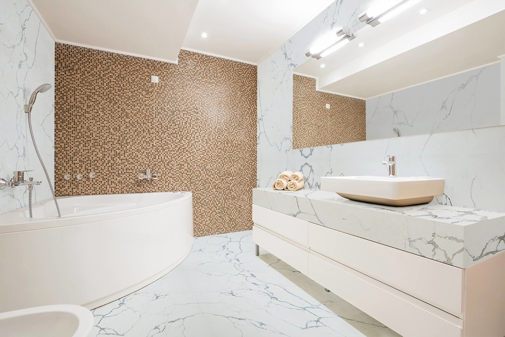 Photo of a contemporary master bathroom in New York with flat-panel cabinets, white cabinets, a corner tub, a shower/bathtub combo, beige tile, brown tile, mosaic tile, multi-coloured walls, a vessel sink and grey floor.