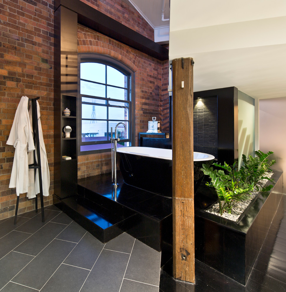 Photo of a mid-sized industrial bathroom in Brisbane with a freestanding tub, black tile and black floor.