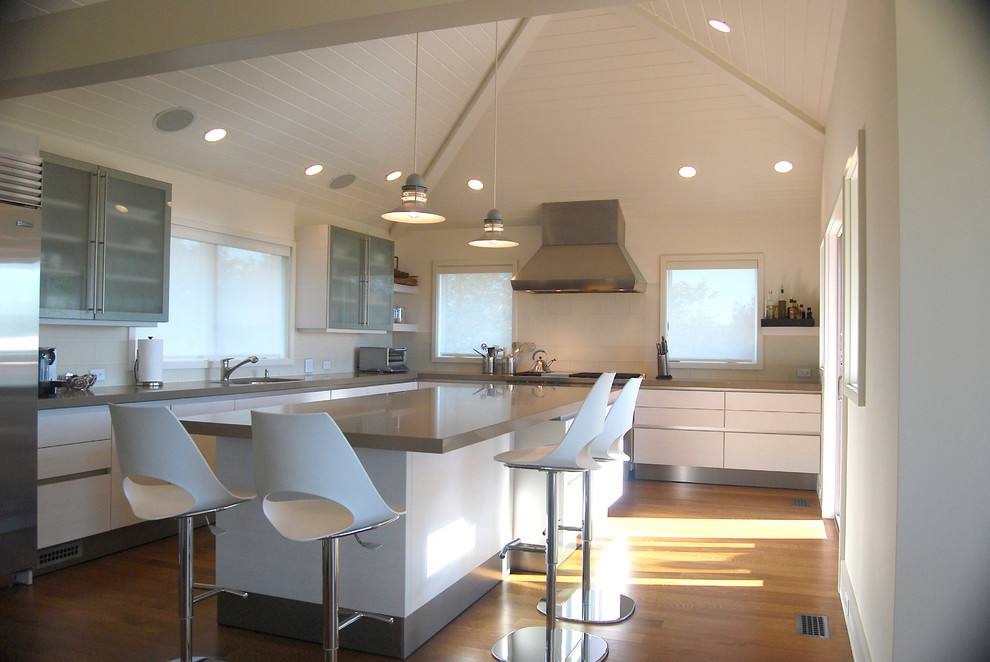 Large modern l-shaped eat-in kitchen in Boston with an undermount sink, flat-panel cabinets, white cabinets, quartz benchtops, white splashback, stainless steel appliances, medium hardwood floors, with island and brown floor.