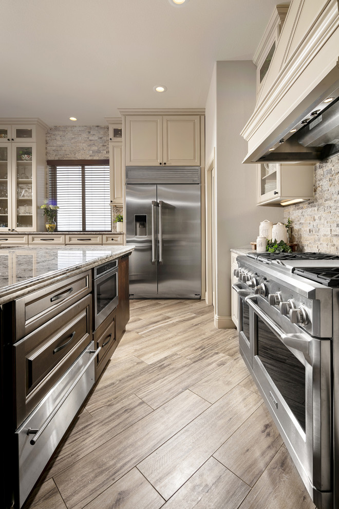 Large transitional l-shaped porcelain tile and brown floor eat-in kitchen photo in Orlando with an undermount sink, raised-panel cabinets, beige cabinets, quartz countertops, multicolored backsplash, travertine backsplash, stainless steel appliances, an island and multicolored countertops