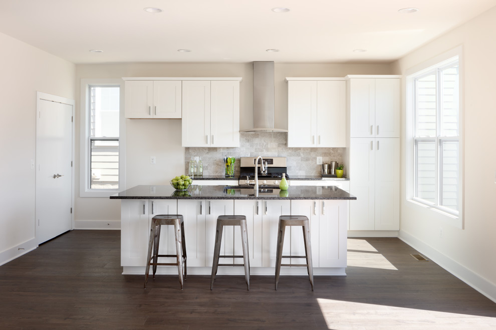 Contemporary single-wall open plan kitchen in Other with an undermount sink, shaker cabinets, white cabinets, granite benchtops, grey splashback, limestone splashback, stainless steel appliances, laminate floors, with island, brown floor and black benchtop.