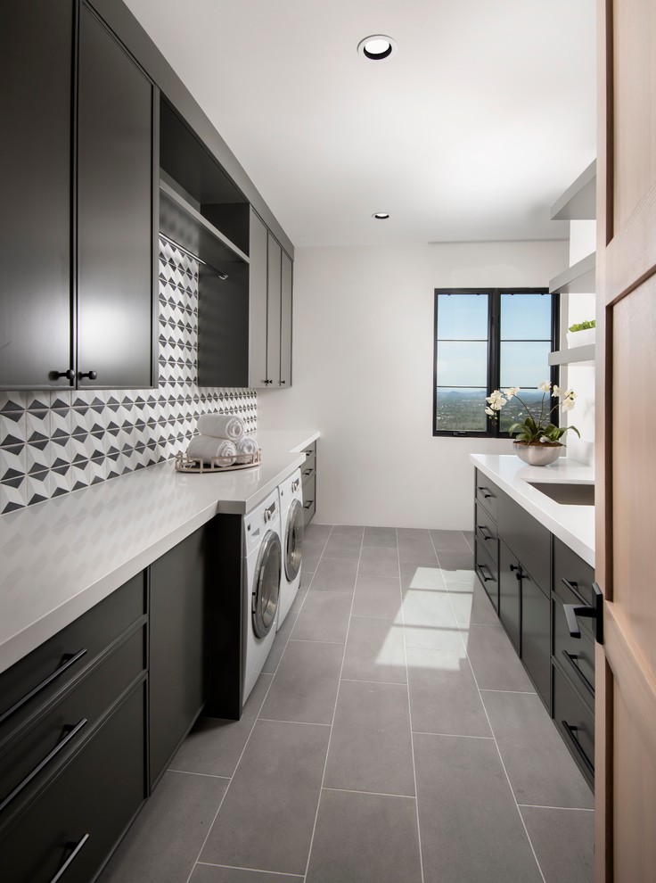 Contemporary l-shaped utility room in Phoenix with black cabinets, white walls, an integrated washer and dryer, grey floor and white benchtop.
