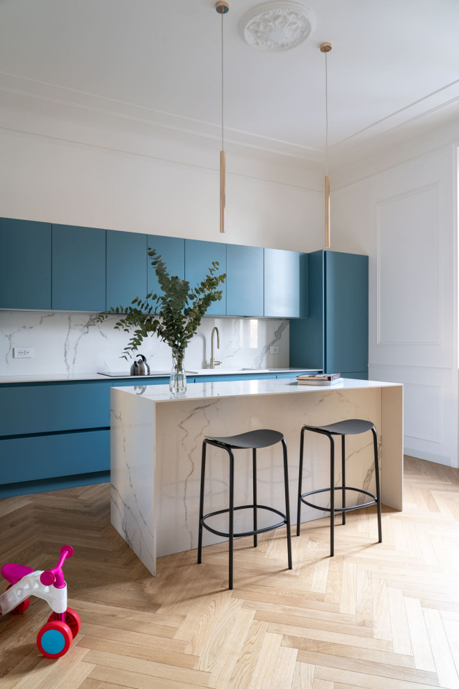 This is an example of a mid-sized traditional galley open plan kitchen in Milan with flat-panel cabinets, blue cabinets, marble benchtops, white splashback, ceramic splashback, light hardwood floors and with island.