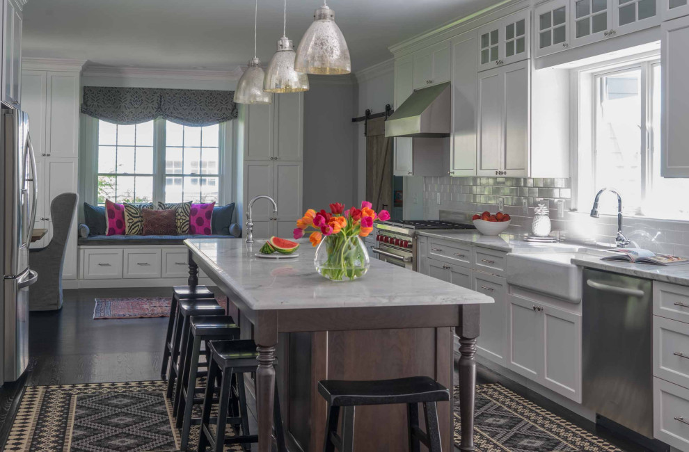 Example of a mid-sized transitional galley dark wood floor and brown floor eat-in kitchen design in Boston with white cabinets, marble countertops, white backsplash, subway tile backsplash, stainless steel appliances, an island and gray countertops