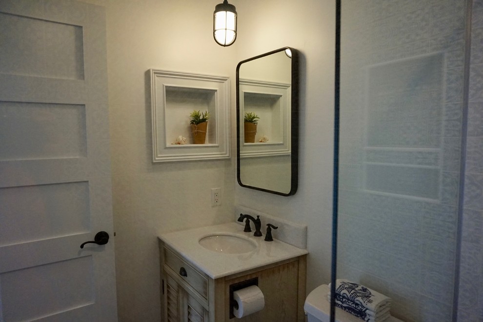 This is an example of a small beach style 3/4 bathroom in Charleston with louvered cabinets, beige cabinets, an alcove shower, a two-piece toilet, blue tile, ceramic tile, white walls, porcelain floors, an undermount sink, engineered quartz benchtops, brown floor, a hinged shower door and white benchtops.