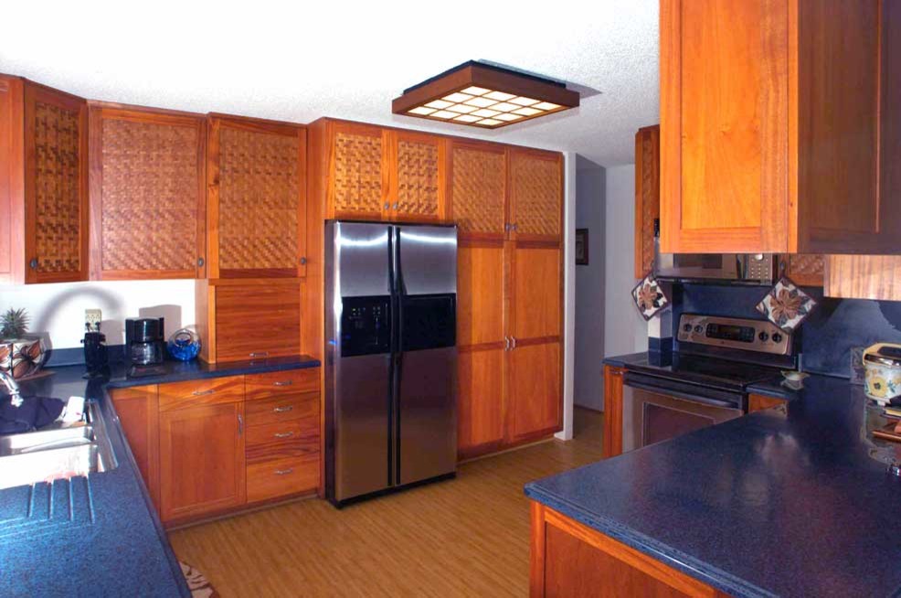 This is an example of a mid-sized tropical kitchen in Hawaii with an undermount sink, shaker cabinets, medium wood cabinets, grey splashback, stainless steel appliances, bamboo floors and no island.