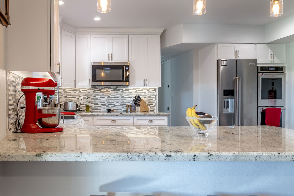 Inspiration for a mid-sized transitional u-shaped laminate floor and brown floor open concept kitchen remodel in Phoenix with an undermount sink, recessed-panel cabinets, white cabinets, granite countertops, multicolored backsplash, mosaic tile backsplash and stainless steel appliances