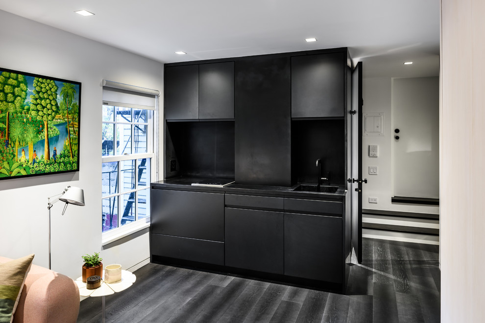 Inspiration for a small modern single-wall eat-in kitchen in New York with an integrated sink, flat-panel cabinets, black cabinets, solid surface benchtops, black splashback, panelled appliances, dark hardwood floors and no island.