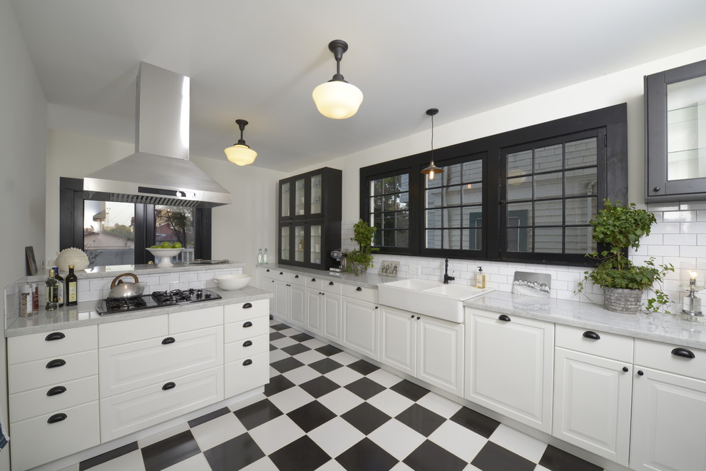 This is an example of a large arts and crafts u-shaped separate kitchen in Los Angeles with a peninsula, raised-panel cabinets, white cabinets, marble benchtops, white splashback, subway tile splashback, black appliances, a farmhouse sink and ceramic floors.