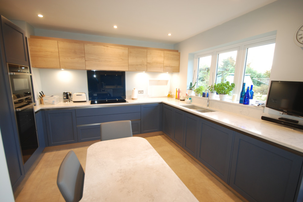 Design ideas for a mid-sized eclectic u-shaped separate kitchen in Surrey with an undermount sink, shaker cabinets, blue cabinets, quartzite benchtops, blue splashback, glass sheet splashback, black appliances, ceramic floors, no island, beige floor and white benchtop.