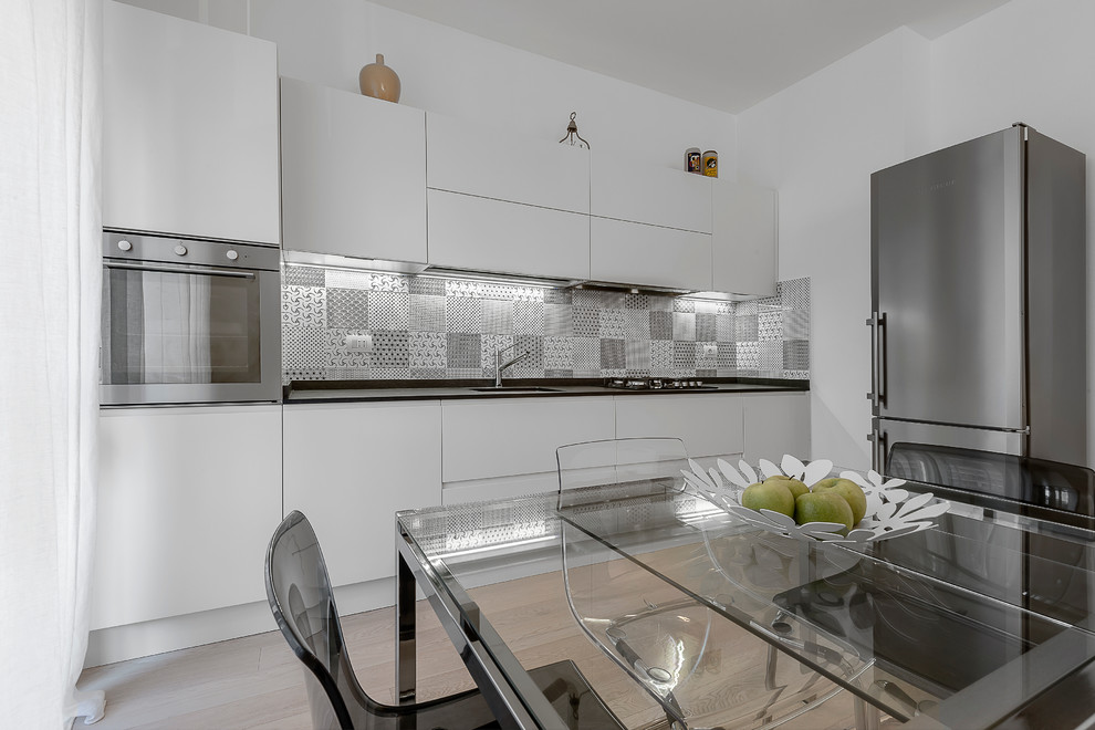 Mid-sized contemporary single-wall eat-in kitchen in Milan with an undermount sink, flat-panel cabinets, white cabinets, multi-coloured splashback, ceramic splashback, stainless steel appliances, ceramic floors and beige floor.