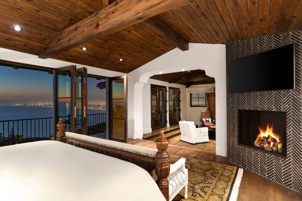 Пример оригинального дизайна: большая спальня в средиземноморском стиле с белыми стенами, паркетным полом среднего тона, горизонтальным камином, фасадом камина из плитки, коричневым полом и деревянным потолком