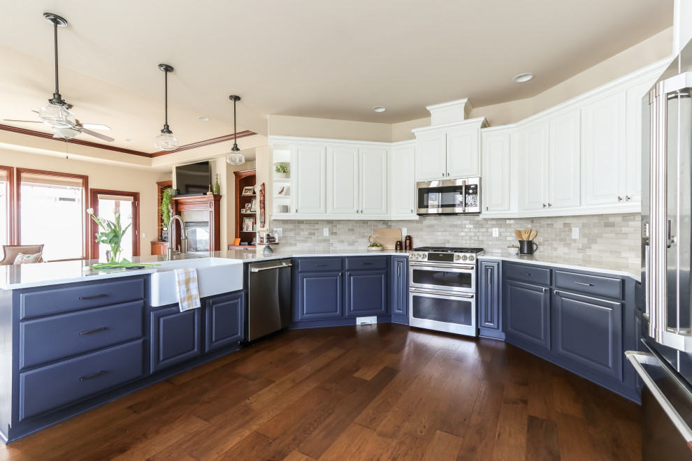 Mid-sized transitional u-shaped medium tone wood floor and brown floor kitchen photo in Seattle with a farmhouse sink, white cabinets, quartz countertops, gray backsplash, marble backsplash, stainless steel appliances and white countertops
