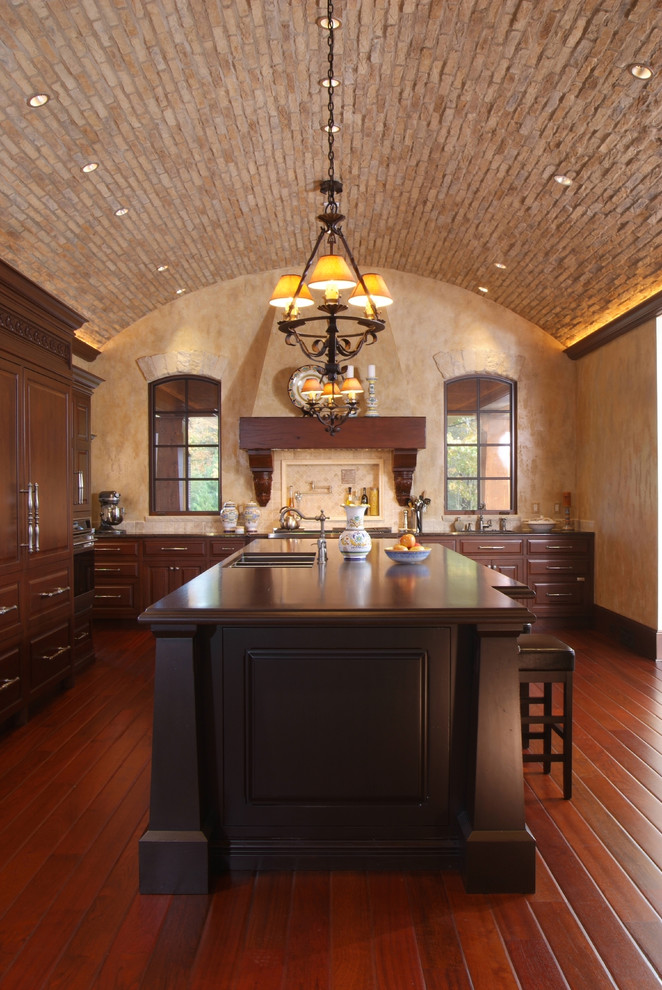 This is an example of a mediterranean kitchen in Grand Rapids with raised-panel cabinets, dark wood cabinets, panelled appliances, an undermount sink and dark hardwood floors.