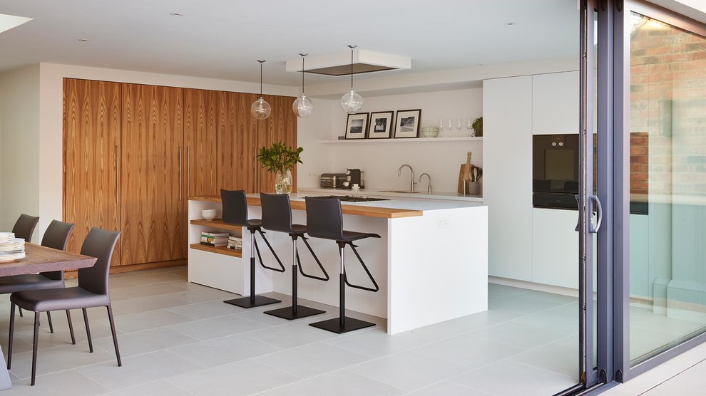 Large scandinavian l-shaped open plan kitchen in London with a submerged sink, recessed-panel cabinets, medium wood cabinets, composite countertops, white splashback, porcelain flooring, an island, white floors and white worktops.