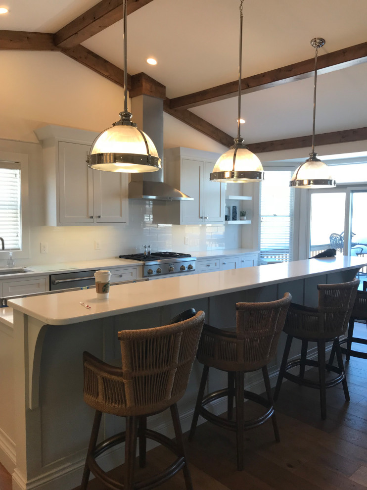 Large transitional l-shaped medium tone wood floor, brown floor and exposed beam eat-in kitchen photo with an undermount sink, recessed-panel cabinets, gray cabinets, quartz countertops, white backsplash, subway tile backsplash, stainless steel appliances, an island and white countertops
