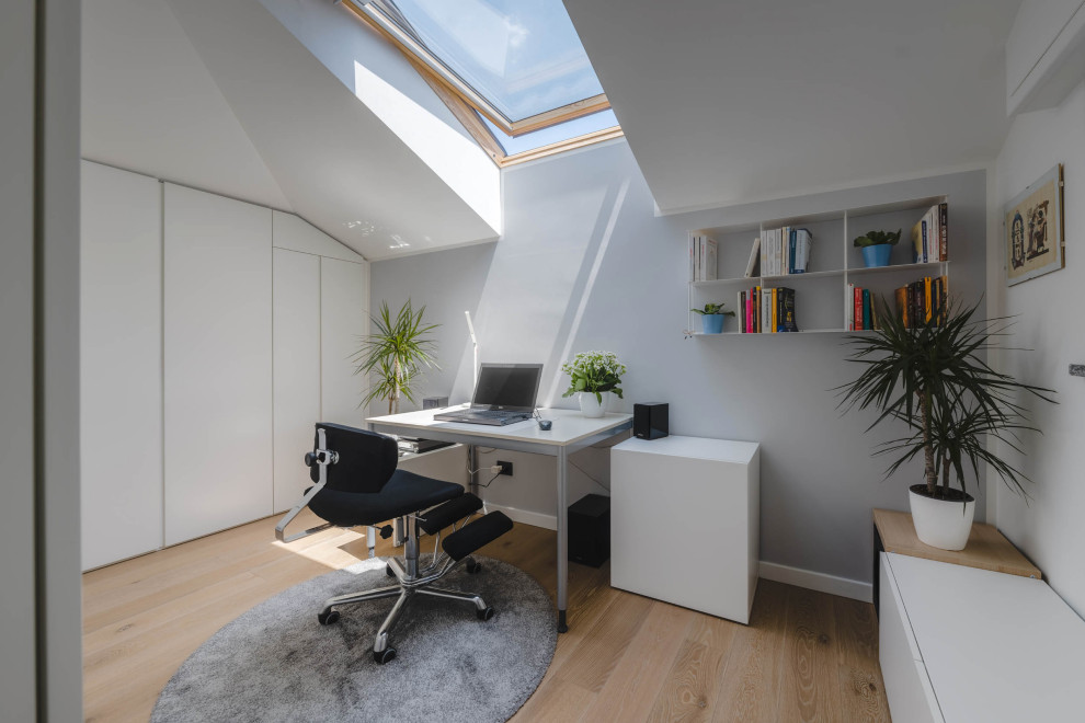 Ejemplo de estudio actual de tamaño medio con paredes grises, suelo de madera clara, escritorio independiente y suelo beige