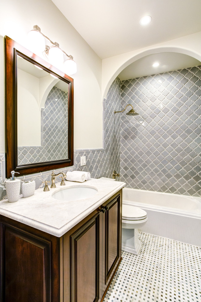 Mediterranean bathroom in Los Angeles with an undermount sink, raised-panel cabinets, dark wood cabinets, an alcove tub, a shower/bathtub combo, gray tile, beige walls and mosaic tile floors.
