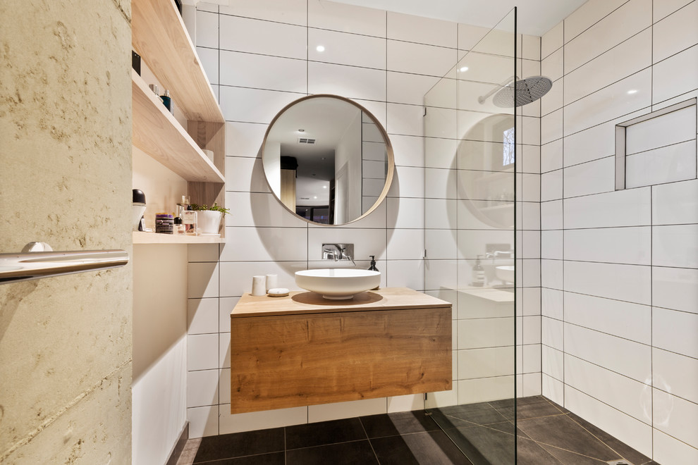 Photo of a small contemporary master wet room bathroom in Melbourne with raised-panel cabinets, medium wood cabinets, a two-piece toilet, white tile, ceramic tile, multi-coloured walls, ceramic floors, a vessel sink, wood benchtops, black floor, an open shower and brown benchtops.