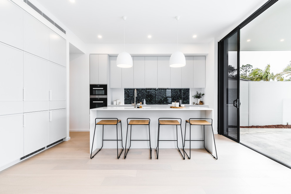 Design ideas for a mid-sized modern l-shaped kitchen in Sydney with flat-panel cabinets, grey cabinets, window splashback, black appliances, light hardwood floors, with island, beige floor and white benchtop.
