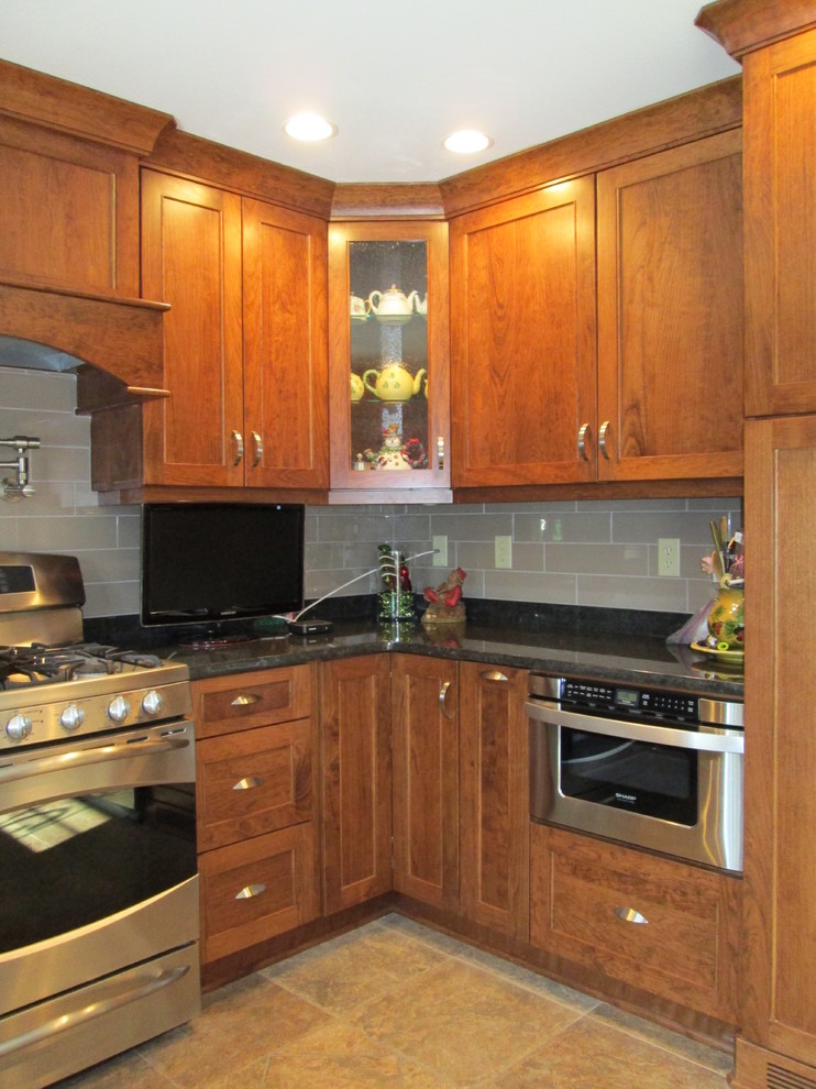 This is an example of a mid-sized traditional u-shaped eat-in kitchen in Other with a single-bowl sink, flat-panel cabinets, medium wood cabinets, granite benchtops, black splashback, porcelain splashback, stainless steel appliances and with island.