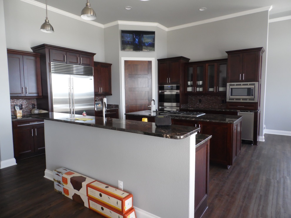 Photo of a large arts and crafts u-shaped open plan kitchen in Austin with recessed-panel cabinets, dark wood cabinets, granite benchtops, multi-coloured splashback, stainless steel appliances, dark hardwood floors and with island.