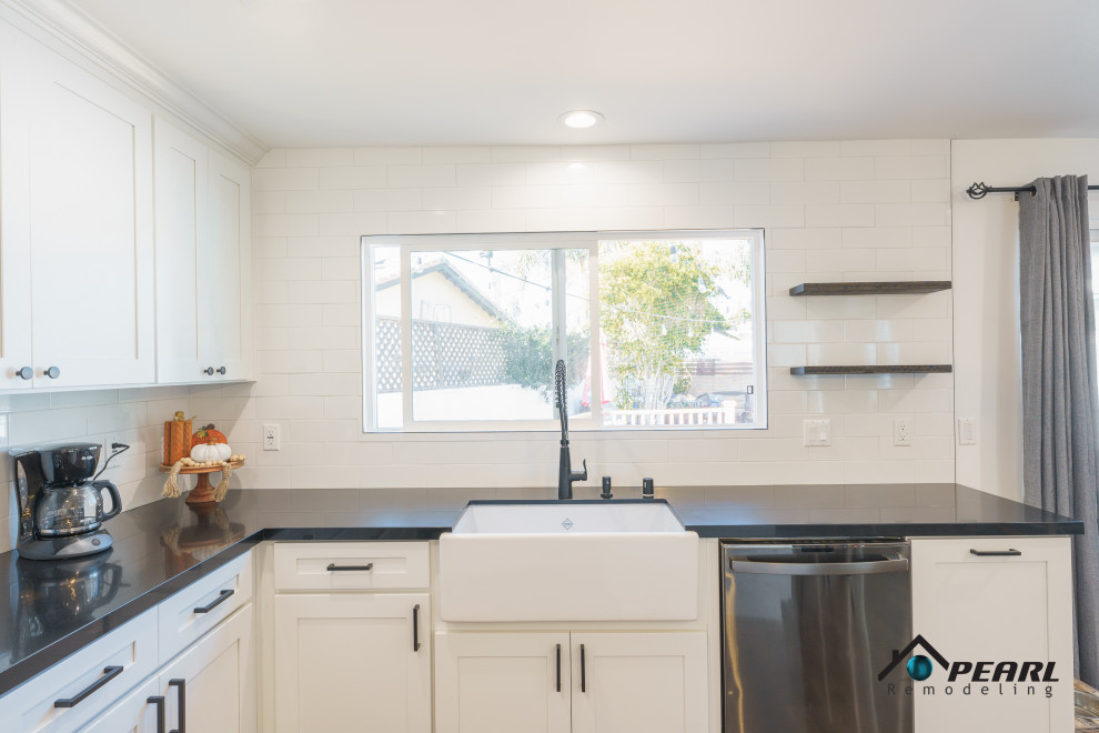 Photo of a large modern l-shaped eat-in kitchen in Los Angeles with a farmhouse sink, shaker cabinets, white cabinets, quartz benchtops, white splashback, subway tile splashback, stainless steel appliances, vinyl floors, with island, brown floor and black benchtop.