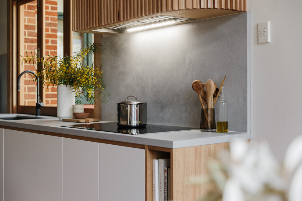 Design ideas for a mid-sized midcentury l-shaped eat-in kitchen in Adelaide with an undermount sink, flat-panel cabinets, black cabinets, solid surface benchtops, grey splashback, stone slab splashback, panelled appliances, light hardwood floors, with island, brown floor and grey benchtop.