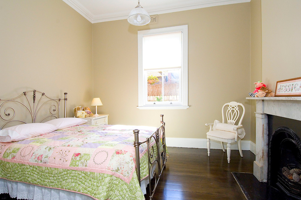This is an example of a traditional bedroom in Sydney with beige walls, dark hardwood floors and a standard fireplace.