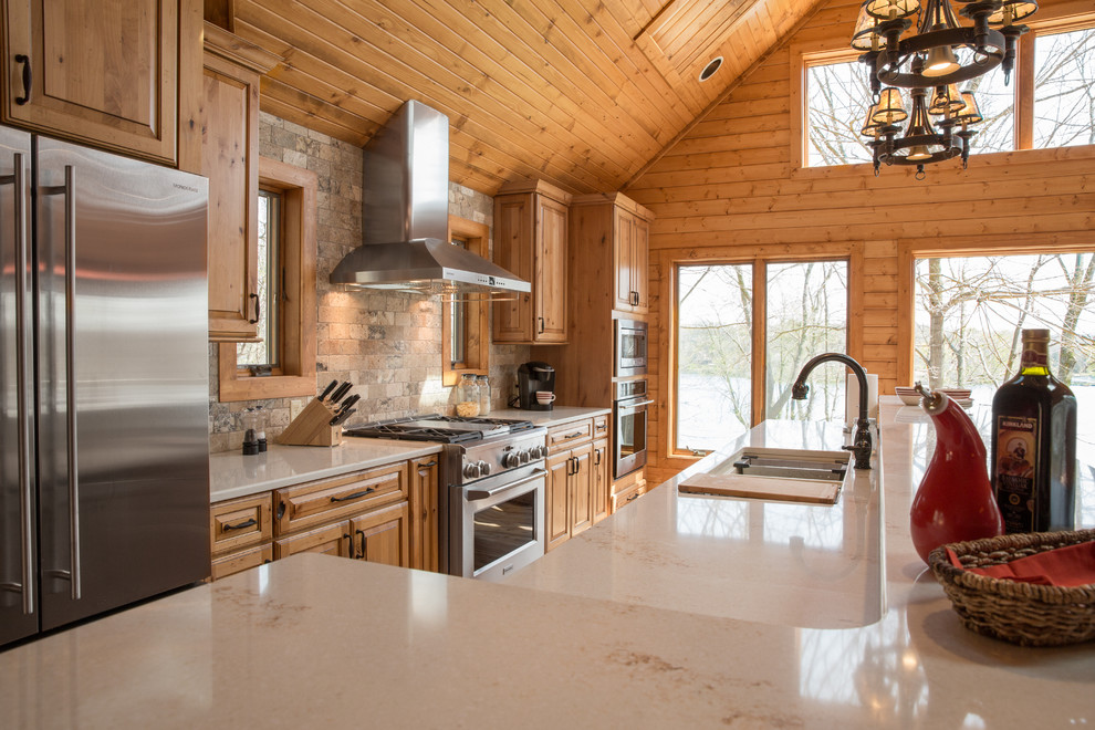 Country open plan kitchen in Milwaukee with an undermount sink, raised-panel cabinets, medium wood cabinets, quartzite benchtops, stainless steel appliances, light hardwood floors and with island.