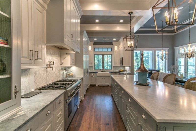 Photo of an expansive arts and crafts u-shaped eat-in kitchen in Houston with a farmhouse sink, raised-panel cabinets, white cabinets, marble benchtops, grey splashback, marble splashback, panelled appliances, dark hardwood floors, with island and brown floor.