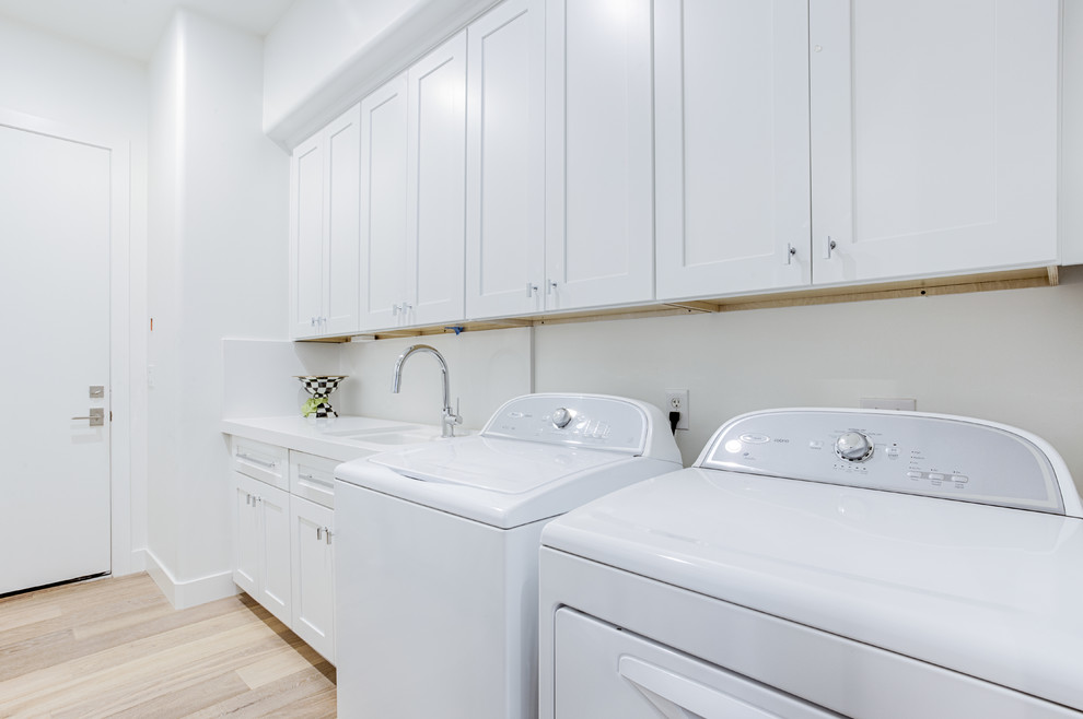 Inspiration for a large transitional galley light wood floor dedicated laundry room remodel in Phoenix with an undermount sink, shaker cabinets, white cabinets, quartz countertops, white walls and a side-by-side washer/dryer