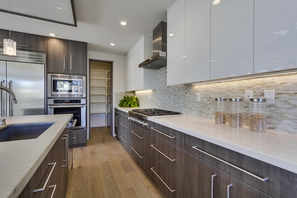 Large contemporary l-shaped open plan kitchen in Los Angeles with flat-panel cabinets, medium wood cabinets, quartz benchtops, multi-coloured splashback, mosaic tile splashback, stainless steel appliances, light hardwood floors and with island.