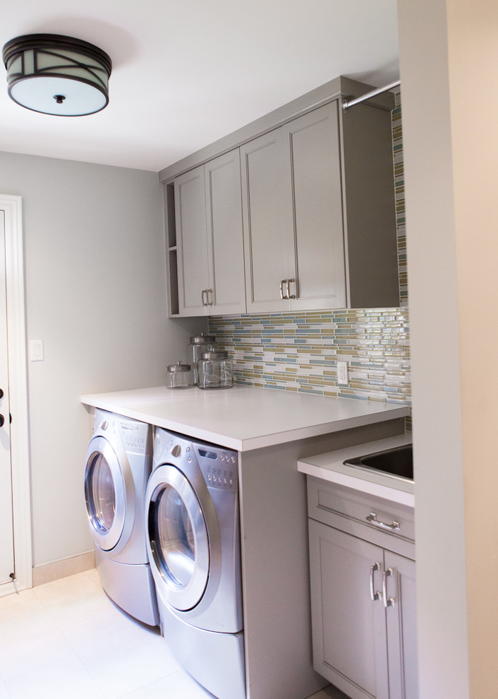 Small transitional galley utility room in Toronto with an utility sink, shaker cabinets, grey cabinets, laminate benchtops, grey walls, ceramic floors and a side-by-side washer and dryer.
