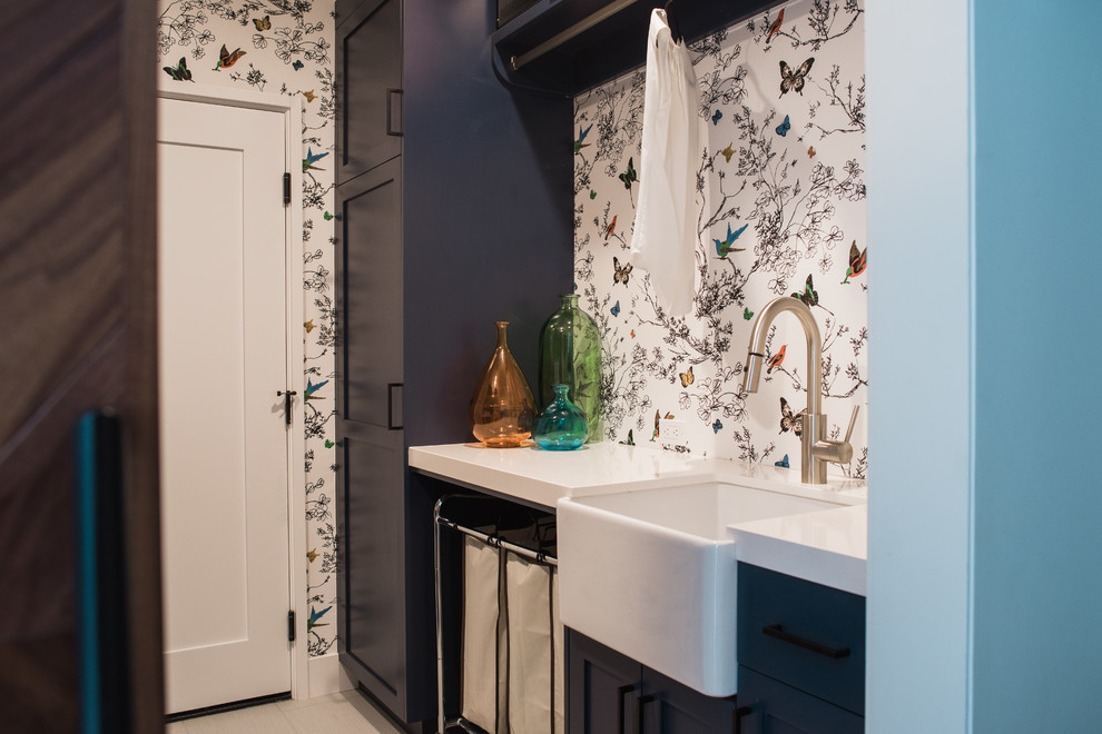 This is an example of a transitional galley utility room in San Francisco with a farmhouse sink, shaker cabinets, blue cabinets, quartz benchtops, light hardwood floors and a stacked washer and dryer.
