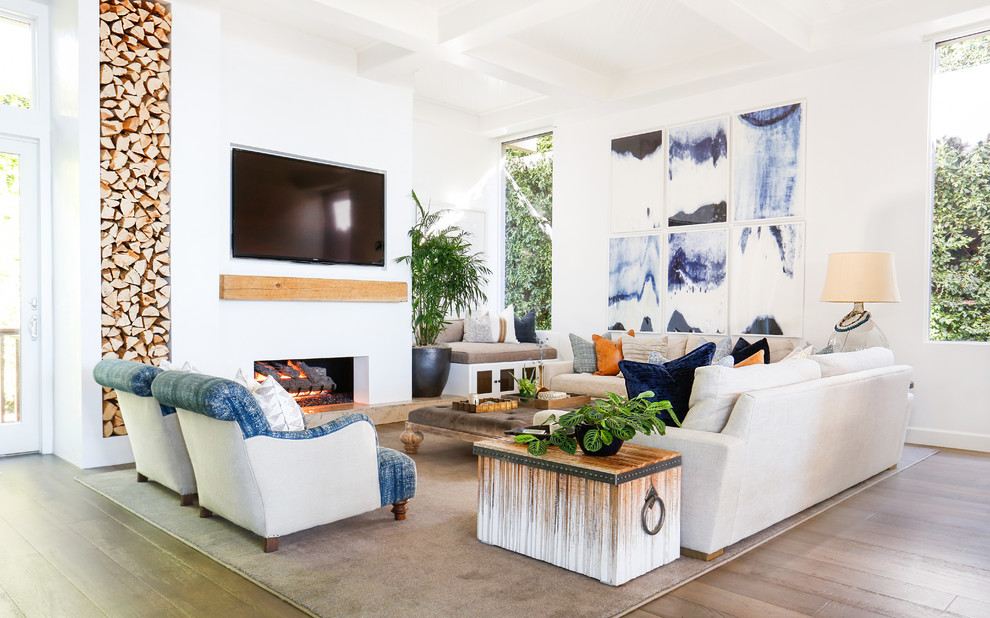 This is an example of a large beach style open concept family room in Orange County with white walls, dark hardwood floors, a ribbon fireplace, a plaster fireplace surround and a wall-mounted tv.