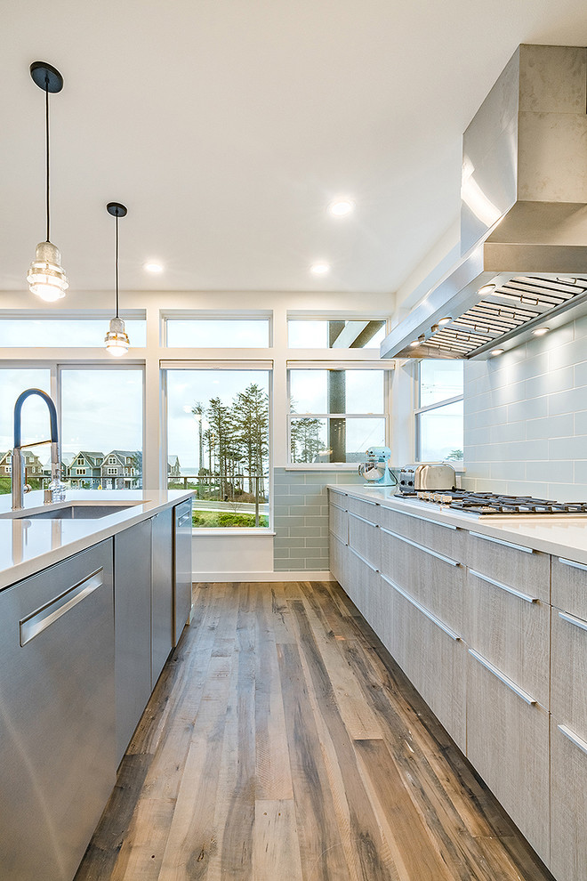 Inspiration for a mid-sized beach style l-shaped open plan kitchen in Seattle with an undermount sink, flat-panel cabinets, light wood cabinets, quartz benchtops, blue splashback, ceramic splashback, stainless steel appliances, medium hardwood floors, with island, brown floor and grey benchtop.