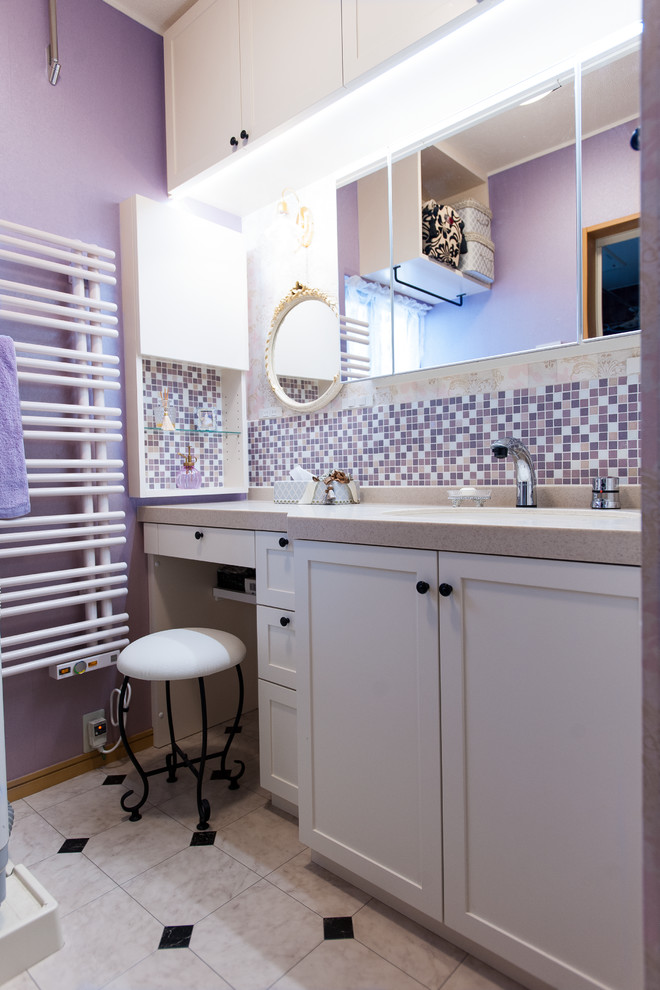 Inspiration for a traditional powder room in Osaka with recessed-panel cabinets, white cabinets, purple walls, multi-coloured floor, pink tile, mosaic tile, an undermount sink, solid surface benchtops, beige benchtops, wallpaper and wallpaper.