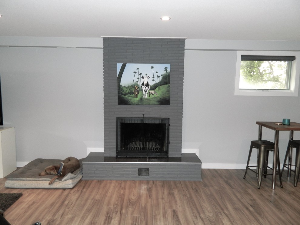 Inspiration for a large contemporary look-out basement in Calgary with grey walls, laminate floors, a standard fireplace, a brick fireplace surround and brown floor.