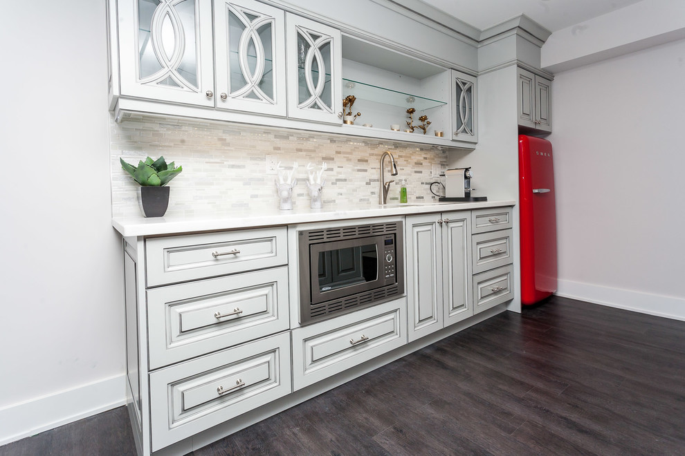 This is an example of a mid-sized contemporary single-wall wet bar in Toronto with an undermount sink, raised-panel cabinets, white cabinets, quartz benchtops, beige splashback, mosaic tile splashback, dark hardwood floors and brown floor.