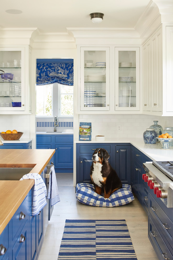 Design ideas for a large beach style kitchen in Other with blue cabinets, white splashback, ceramic splashback, with island, an undermount sink, raised-panel cabinets, stainless steel appliances, light hardwood floors and beige floor.