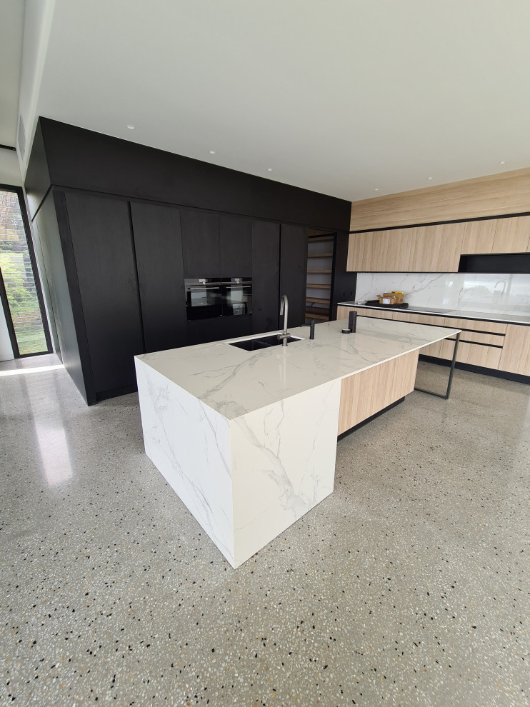 Photo of a medium sized contemporary l-shaped open plan kitchen in Melbourne with a submerged sink, flat-panel cabinets, light wood cabinets, marble worktops, white splashback, marble splashback, black appliances, concrete flooring, an island, grey floors and white worktops.