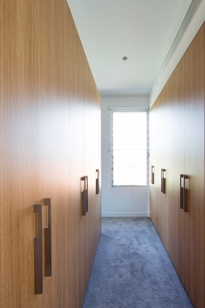 This is an example of a large contemporary gender-neutral walk-in wardrobe in Sydney with light wood cabinets and carpet.