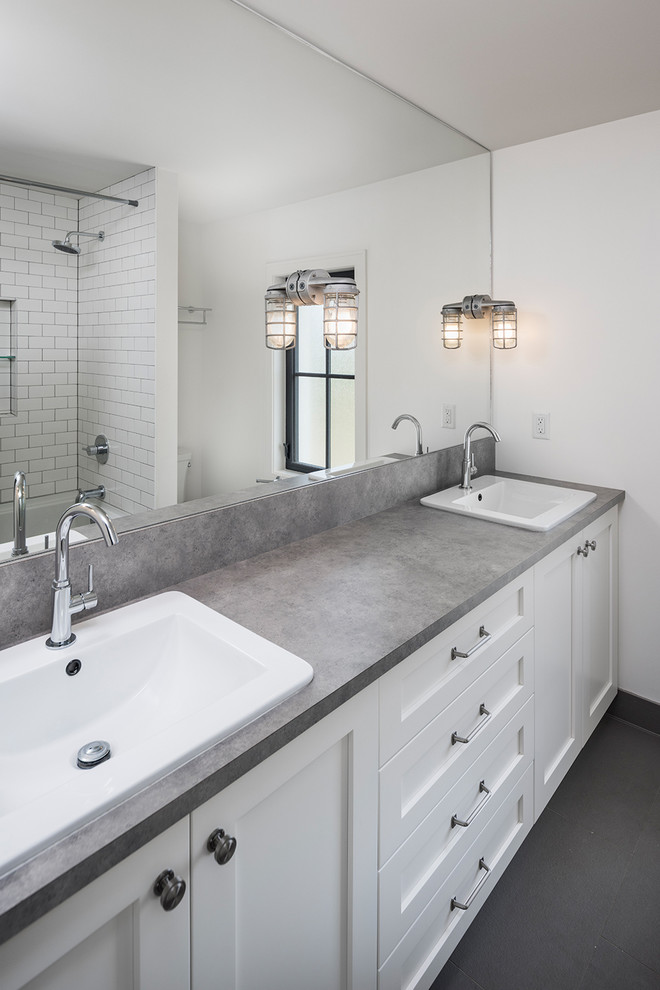 Photo of a mid-sized country master bathroom in Vancouver with shaker cabinets, white cabinets, an alcove tub, a two-piece toilet, grey walls, ceramic floors, a drop-in sink, laminate benchtops, grey floor, a shower curtain and a shower/bathtub combo.