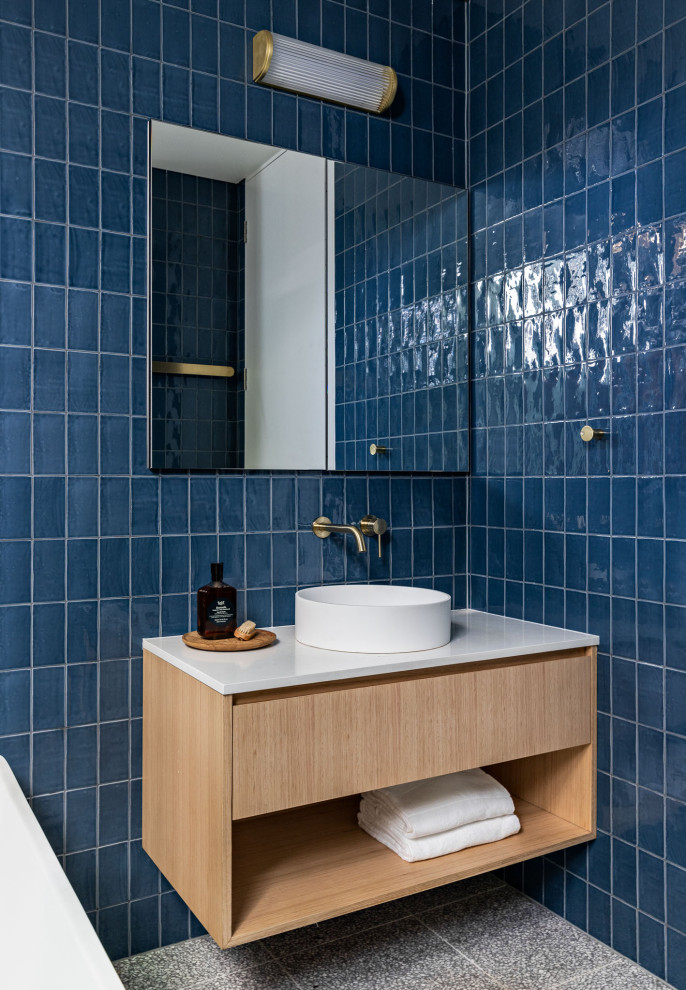 Идея дизайна: маленькая главная ванная комната в современном стиле с открытыми фасадами, светлыми деревянными фасадами, отдельно стоящей ванной, открытым душем, синей плиткой, керамической плиткой, синими стенами, полом из терраццо, столешницей из искусственного кварца, открытым душем, белой столешницей, тумбой под одну раковину, подвесной тумбой и серым полом для на участке и в саду