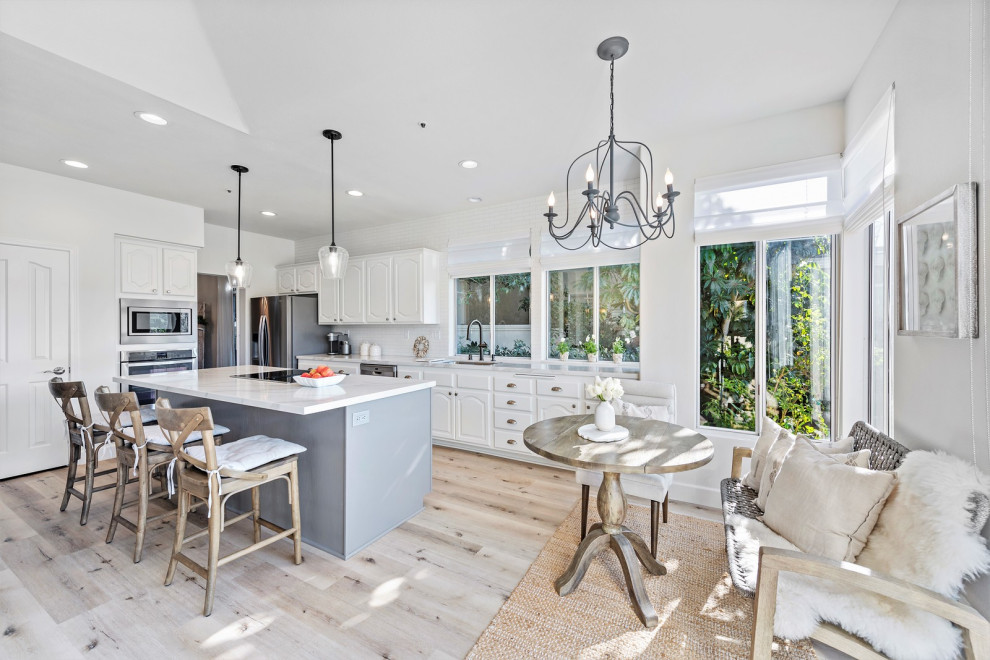 This is an example of a medium sized coastal single-wall kitchen/diner in Orange County with a submerged sink, raised-panel cabinets, white cabinets, engineered stone countertops, white splashback, ceramic splashback, stainless steel appliances, vinyl flooring, an island, beige floors and white worktops.