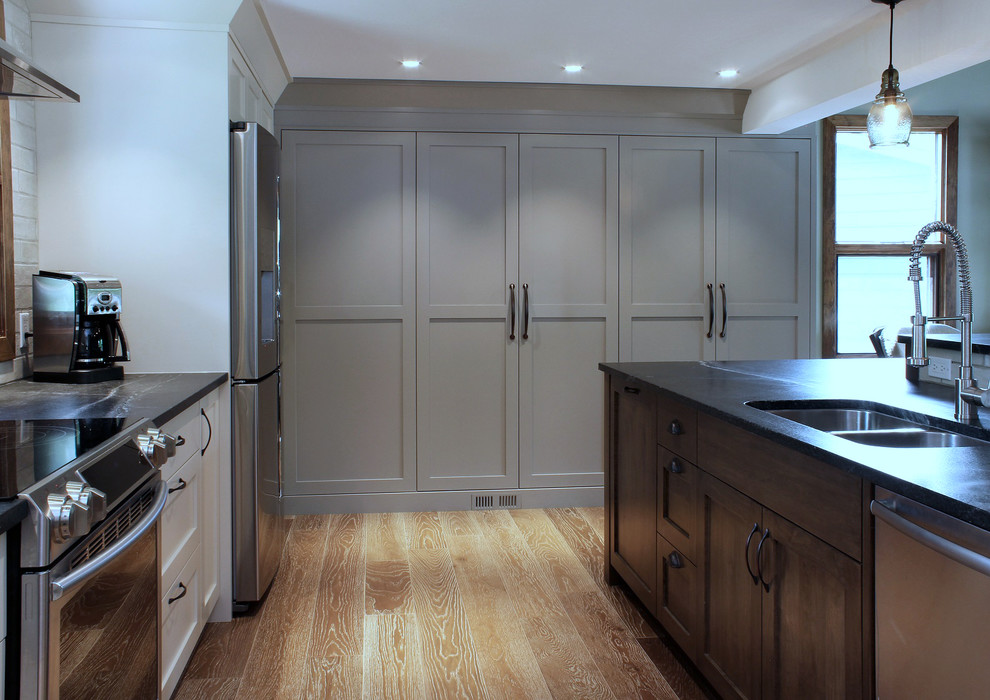 Example of a large transitional u-shaped medium tone wood floor open concept kitchen design in Calgary with an undermount sink, shaker cabinets, soapstone countertops, ceramic backsplash, stainless steel appliances and an island