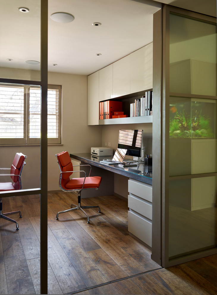 This is an example of a contemporary study room in London with no fireplace, a built-in desk and dark hardwood floors.
