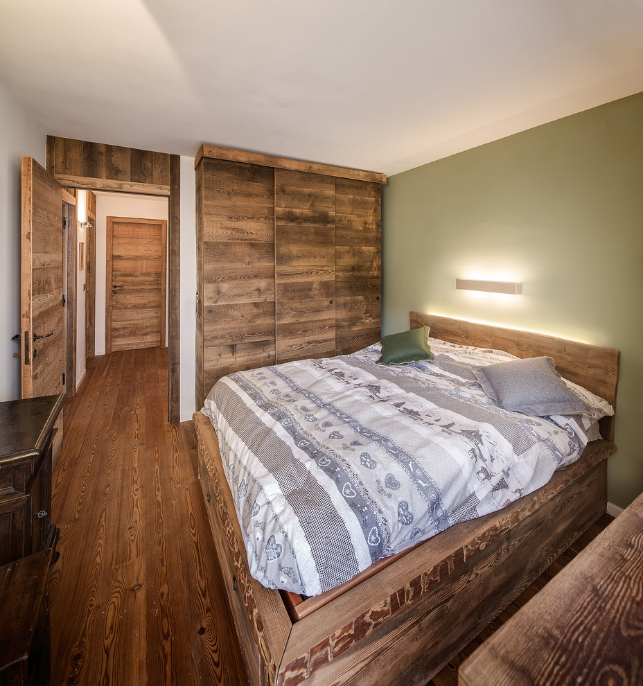 This is an example of a mid-sized country master bedroom in Turin with green walls, medium hardwood floors, no fireplace and brown floor.